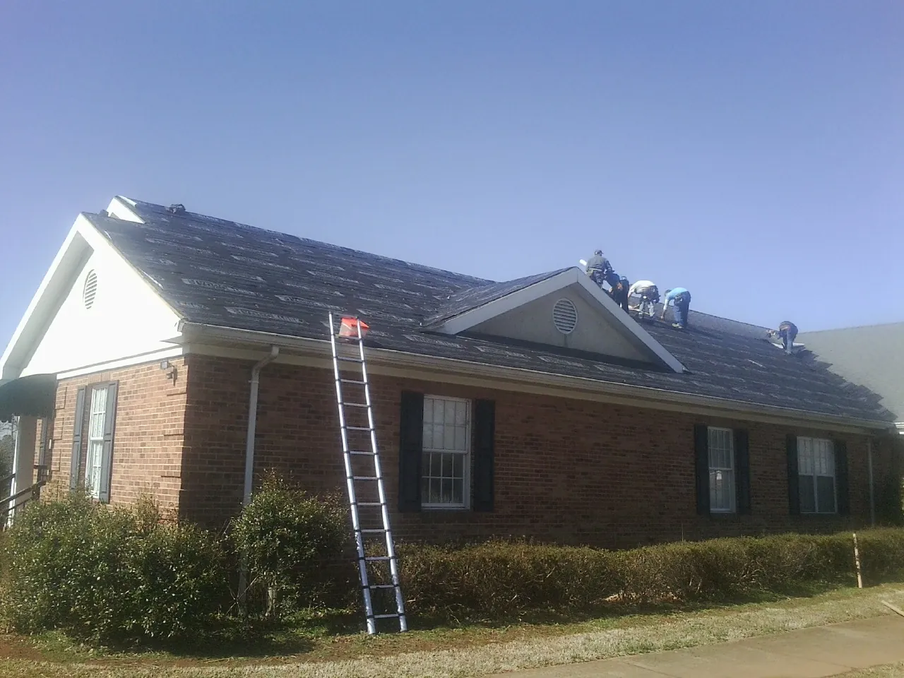 Crew tearing shingles off a brick ranch roof with a ladder set — Emergency Roof Repair work by our crew in Scandinavia