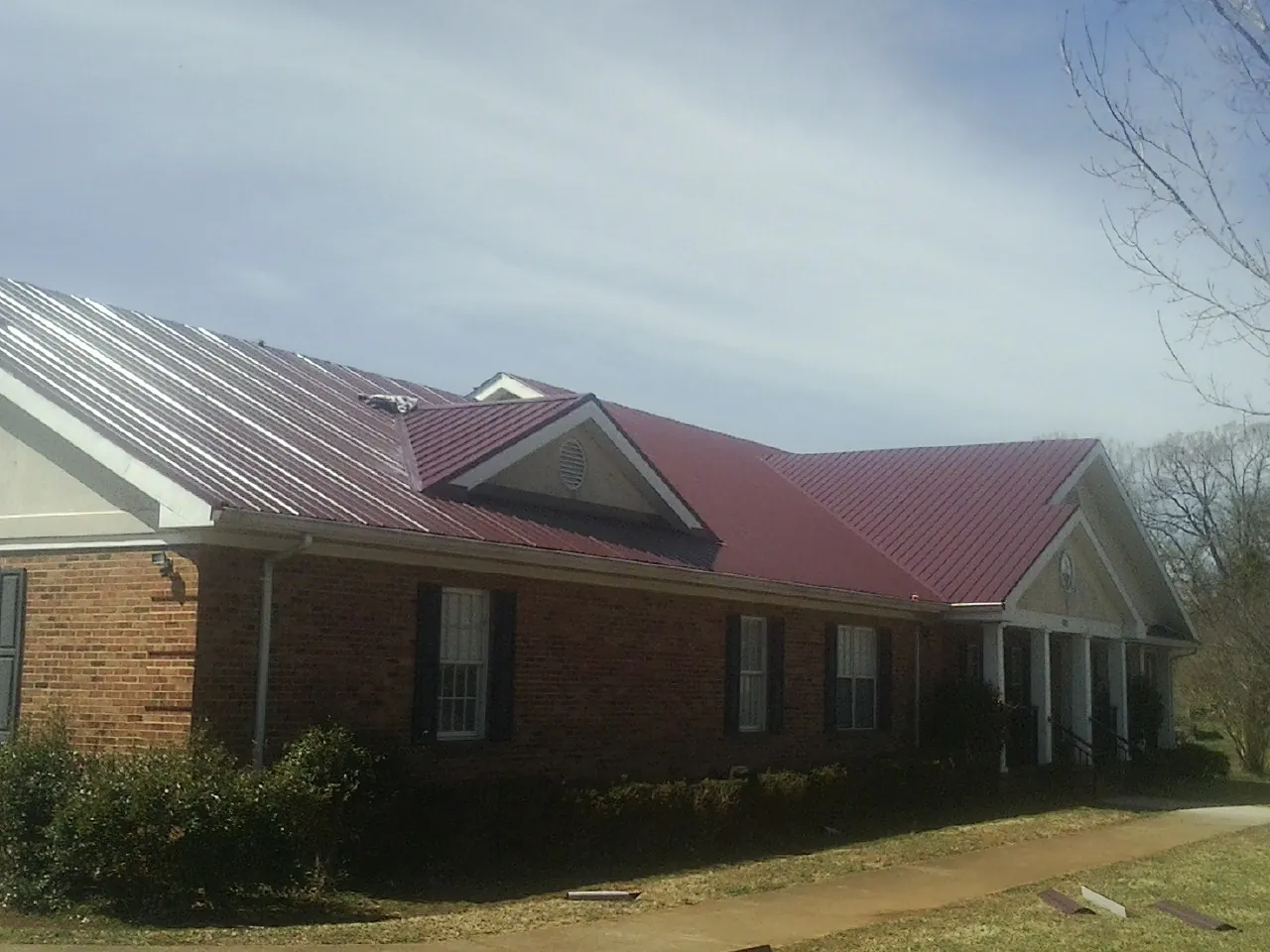Red metal roof with gabled entries on a long brick building, from a Hail Damage Roof Repair job in Scandinavia