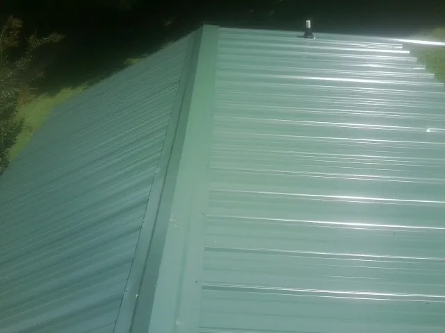 New green metal panels meeting at the ridge of a roof — Flat Roof Repair work by our crew in Scandinavia