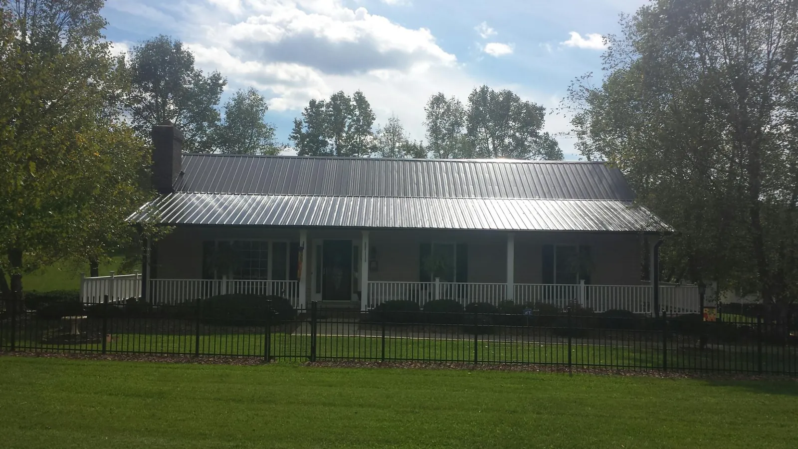 Gray metal roof on a brick ranch with a full width front porch — Gutter Guard Installation work by our crew in Scandinavia
